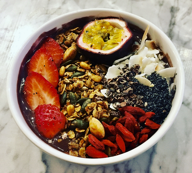 A colourful acai bowl with strawberries, passion fruit and chia seeds on a marble table